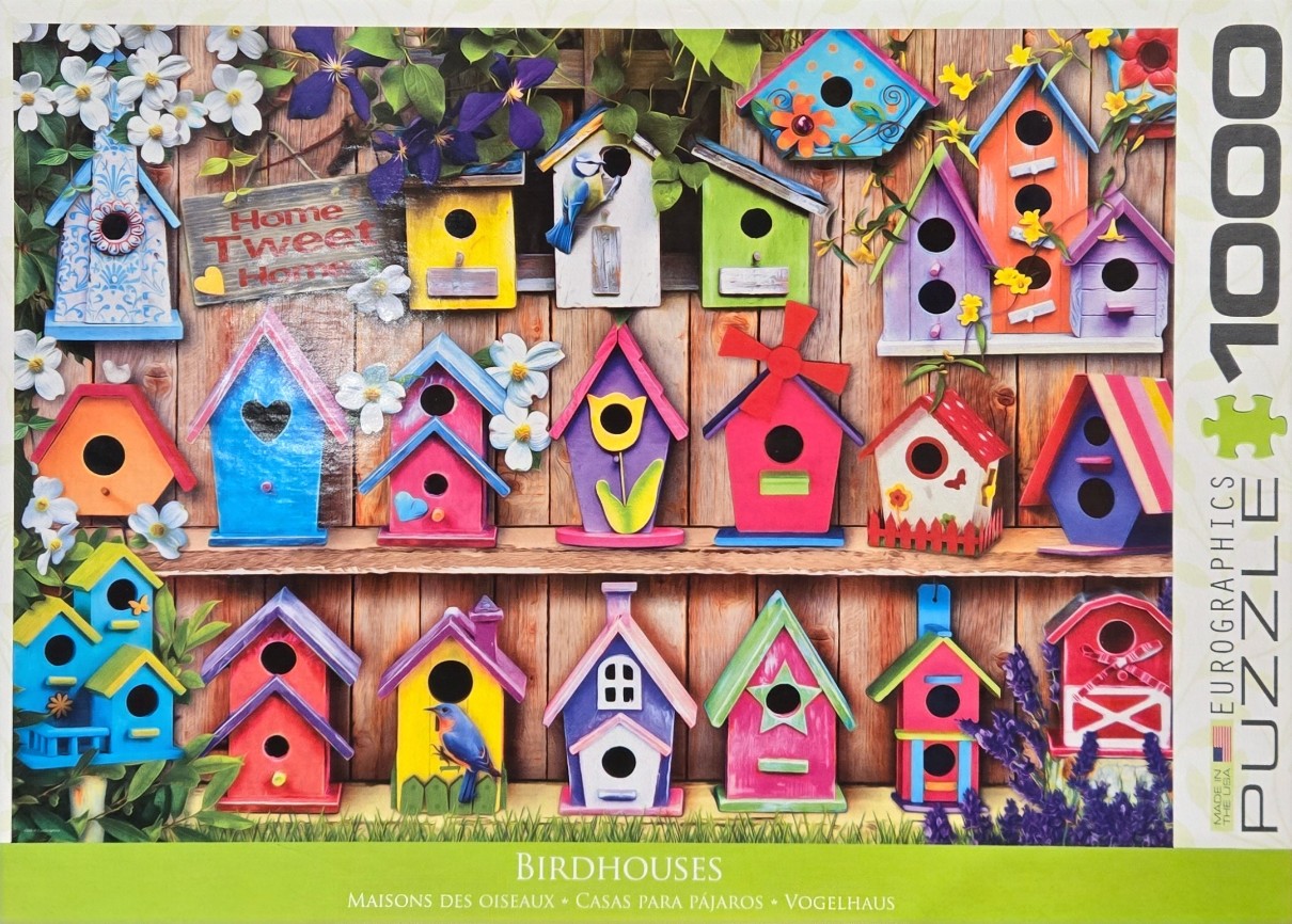A collection of colorful, whimsically designed birdhouses arranged on wooden shelves against a weathered fence.