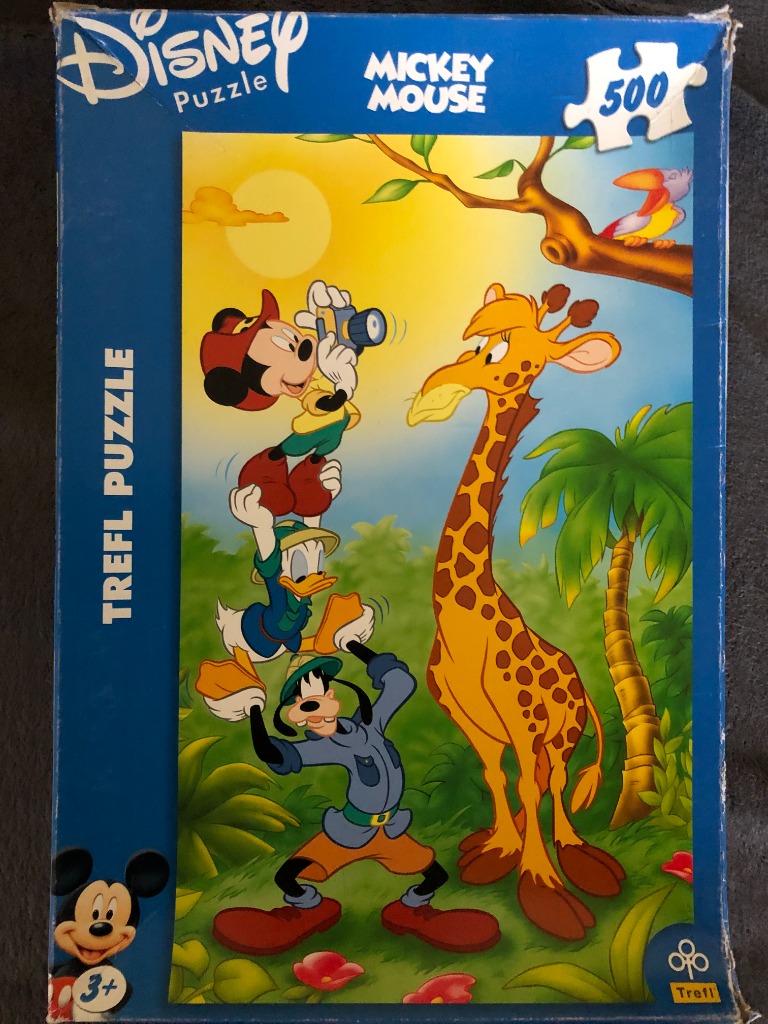 Mickey Mouse, Donald Duck, and Goofy in a totem pole stack taking a photo of a giraffe in a jungle setting.
