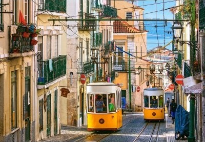 Two vintage yellow trams traveling along a narrow, cobblestone street in a historic European city.