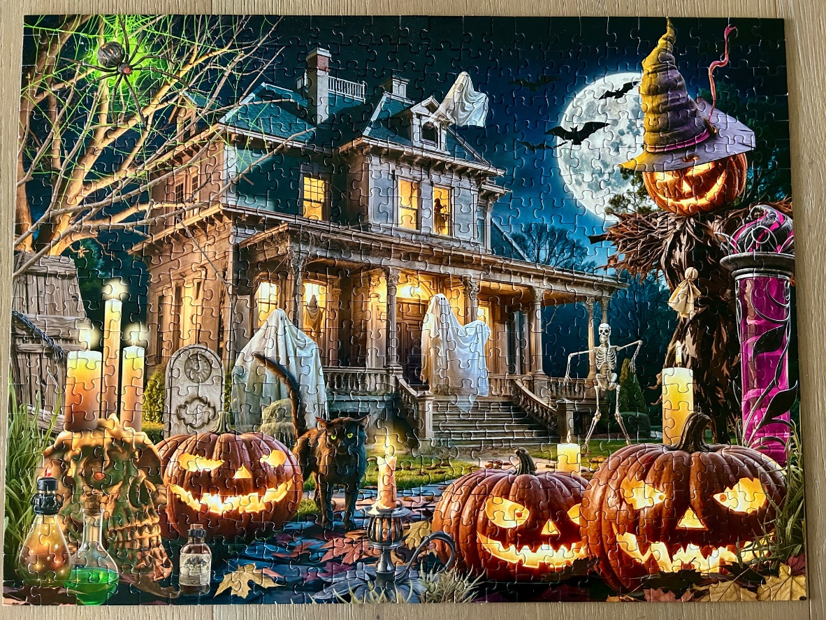 A spooky Victorian haunted house at night surrounded by Halloween decorations like pumpkins, ghosts, and a scarecrow.