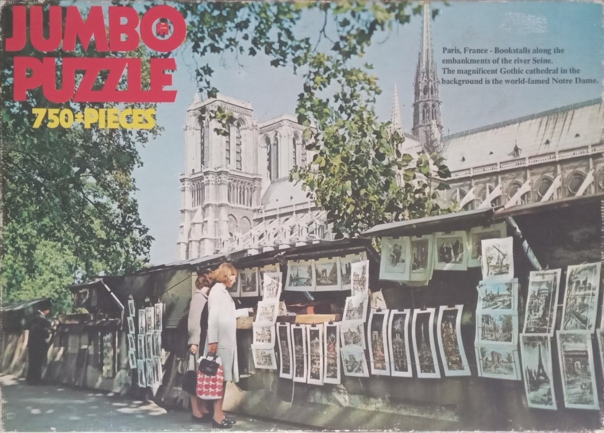 A vintage photograph of Notre Dame cathedral viewed behind bookstalls along the Seine in Paris, France.
