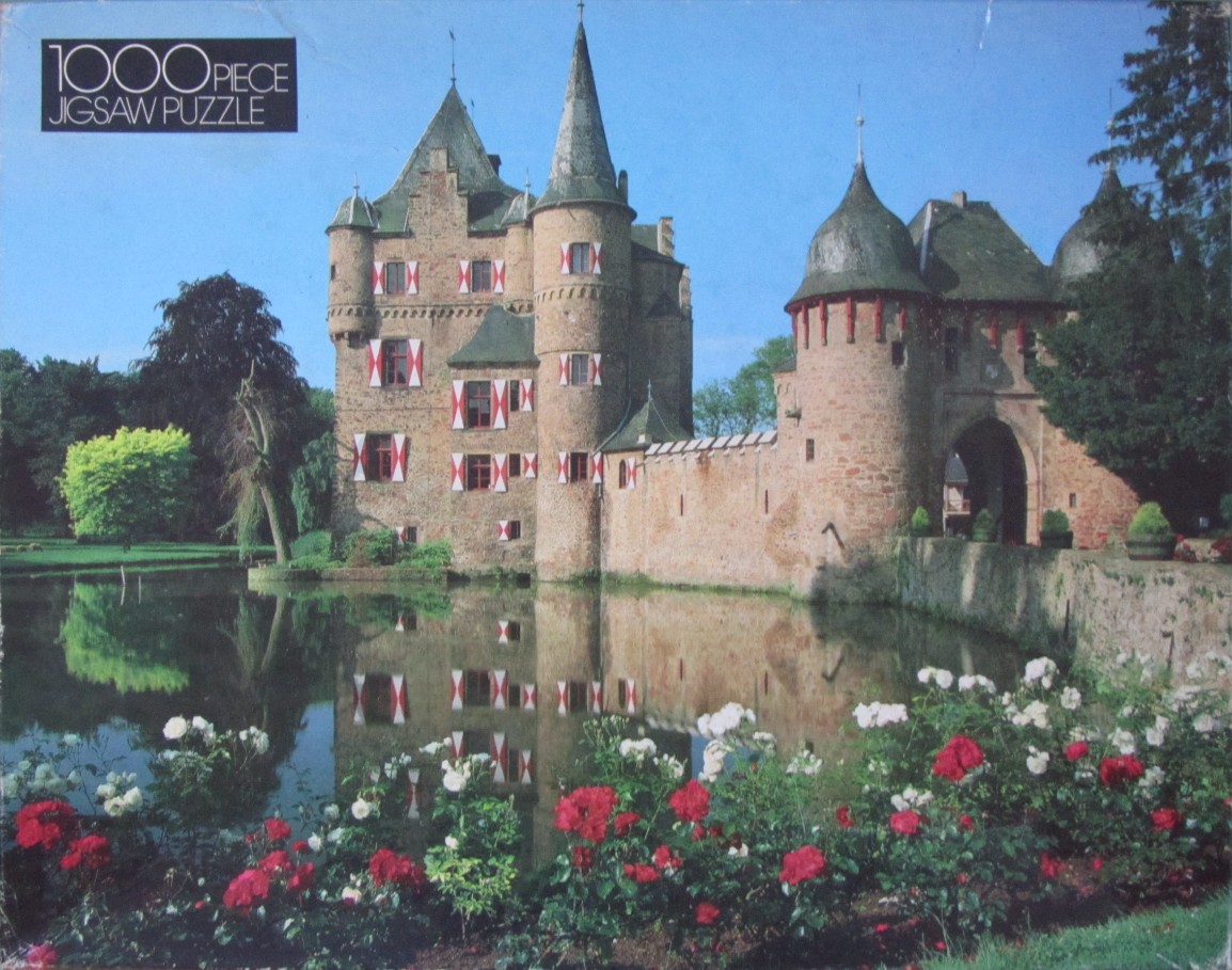 A medieval stone castle with red-and-white shuttered windows, surrounded by a moat and a vibrant flower garden.