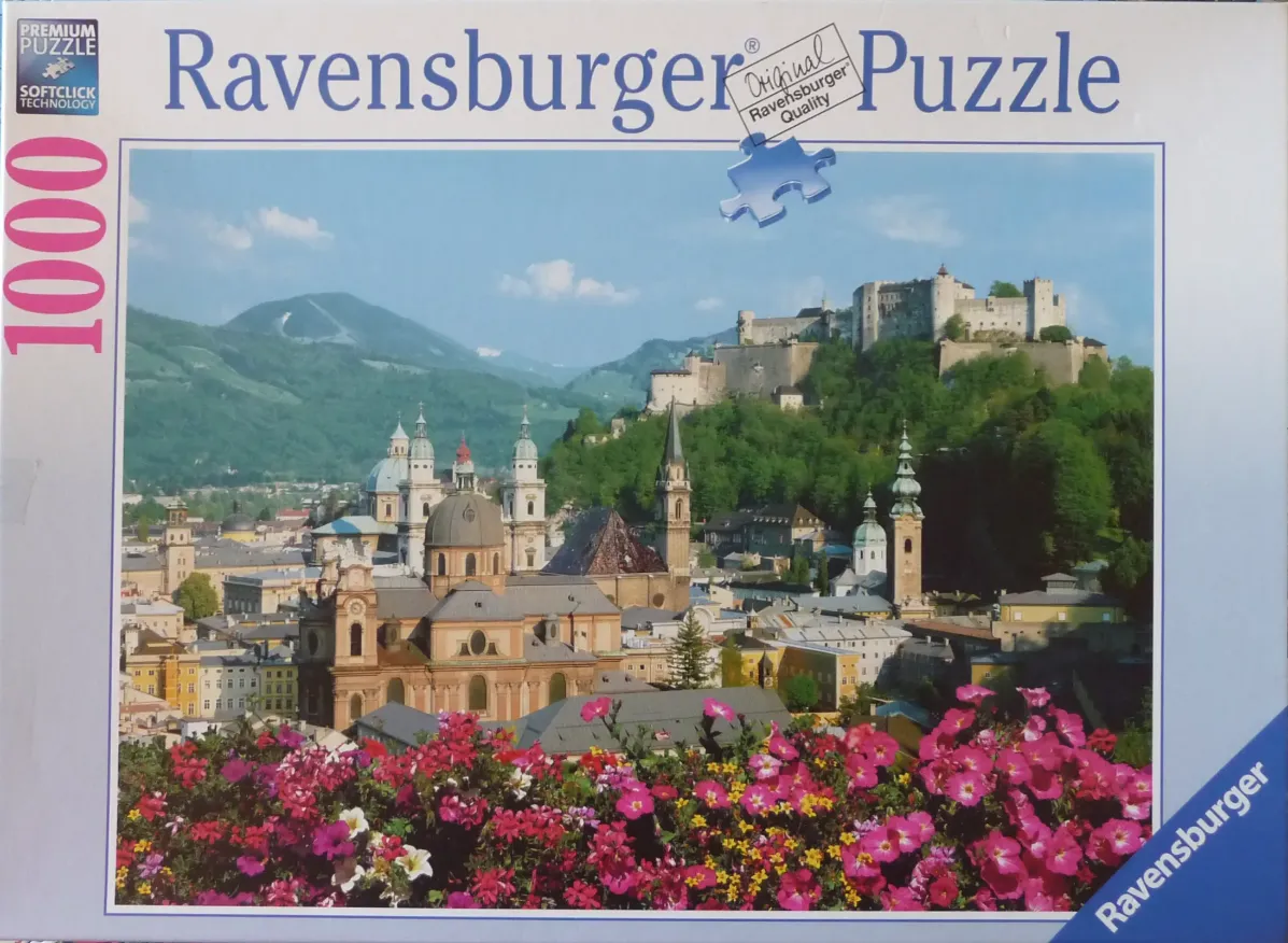 Panoramic view of Salzburg, Austria, with a fortress on a hill and bright pink flowers in the foreground.