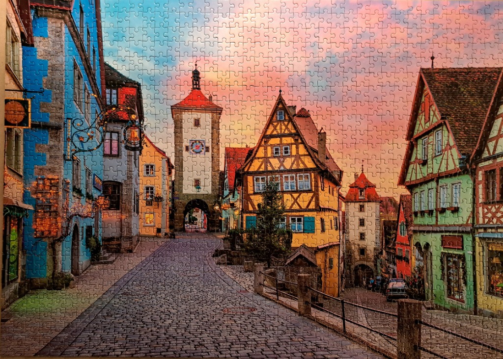 Cobblestone street scene in a historic European town at sunset featuring timber-framed buildings and a clock tower.