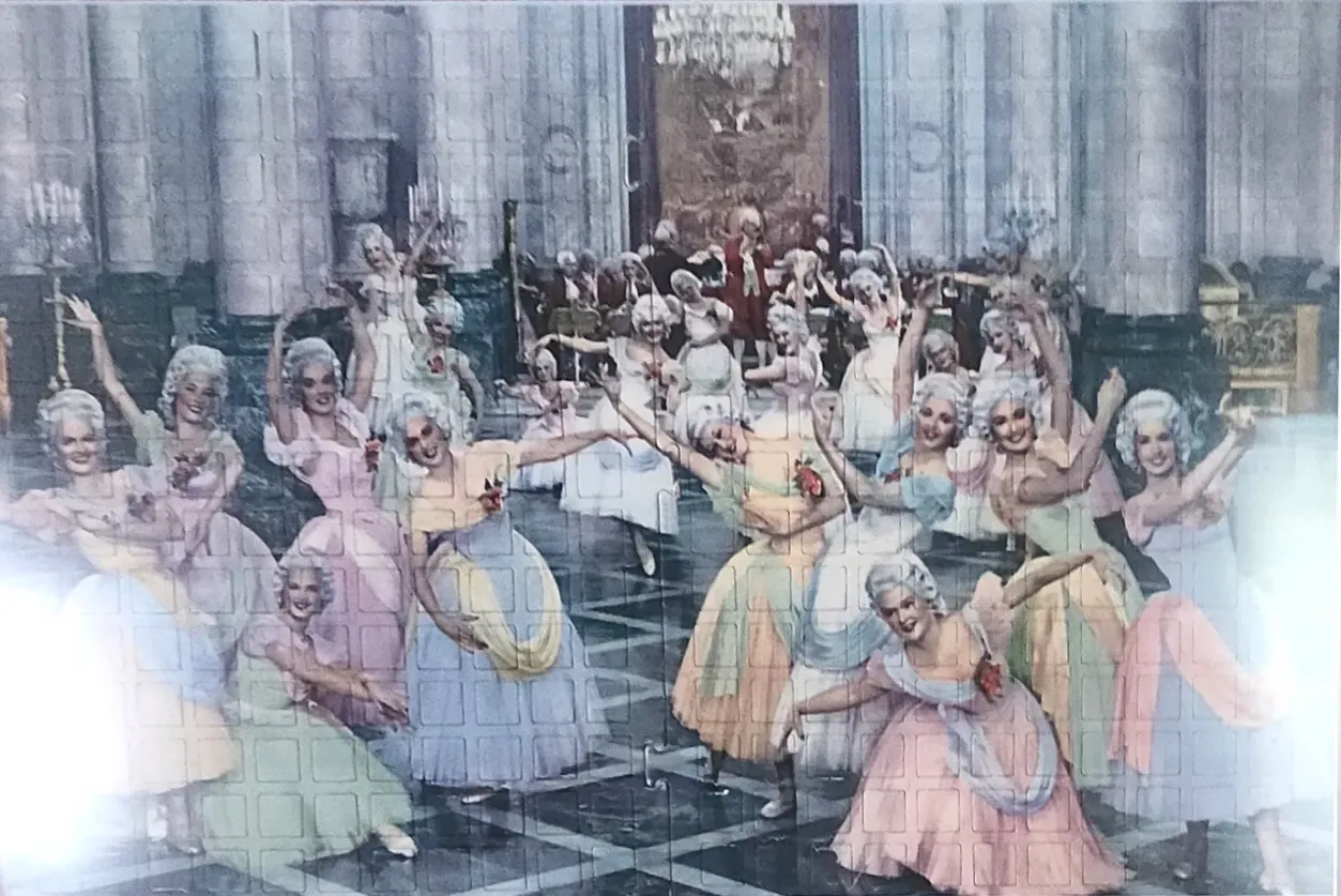 A group of dancers in rococo-style ballgowns and powdered wigs performing in an ornate, palatial hall.