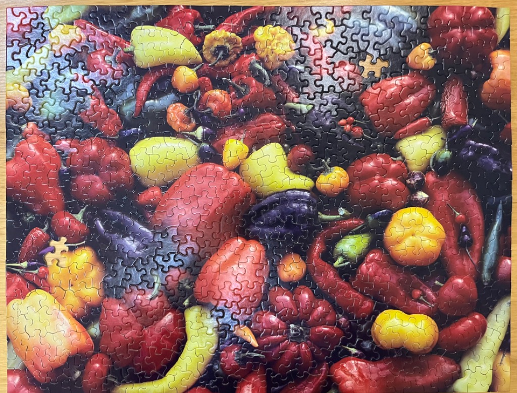 A vibrant, overhead collection of various fresh peppers in red, yellow, and deep purple tones.