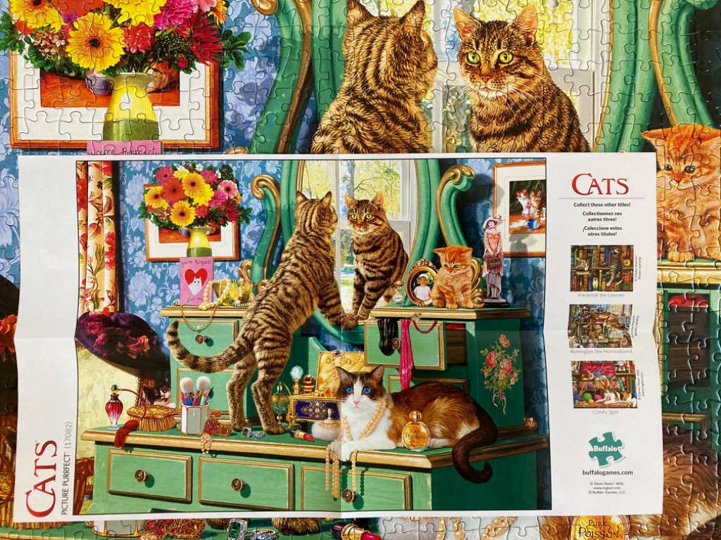 A green vanity table populated by three cats surrounded by perfume bottles, jewelry, and flowers.