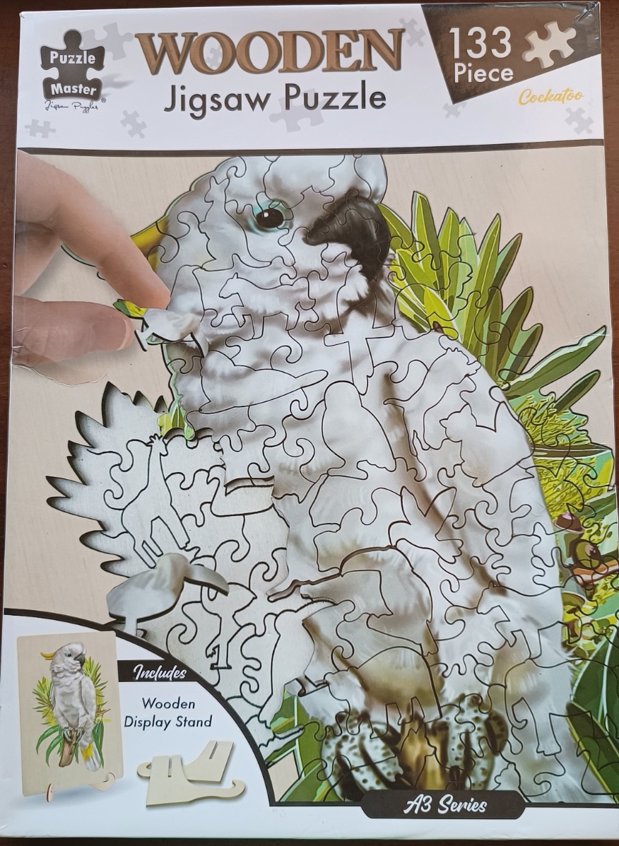 A partial wooden jigsaw puzzle featuring a white sulphur-crested cockatoo against a background of green foliage.