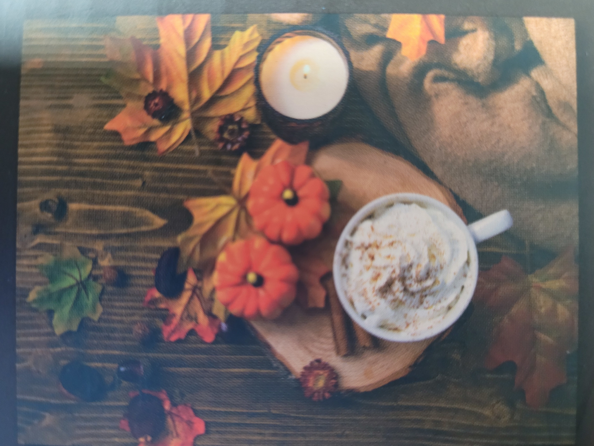 Overhead view of a cup of whipped cream coffee, mini pumpkins, and autumn leaves on a rustic wooden table.