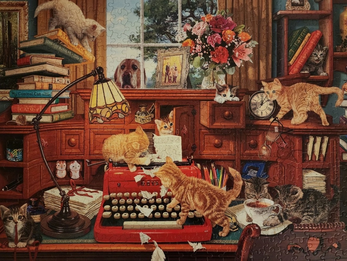 A cozy study filled with kittens playing around a red typewriter and wooden desk.