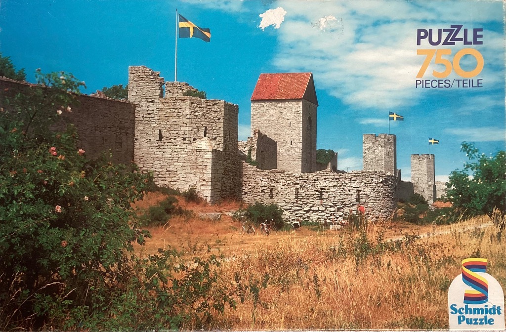 Ancient stone castle wall and towers with Swedish flags under a bright blue sky