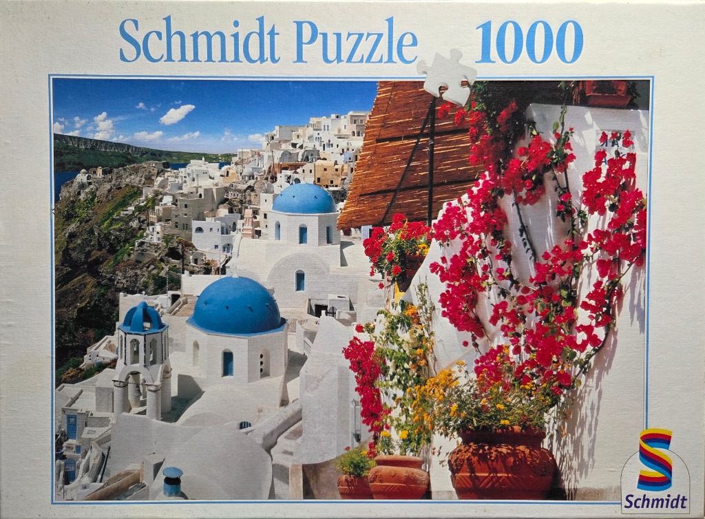 A scenic view of white buildings with blue domes in Santorini, Greece, decorated with vibrant red bougainvillea flowers.