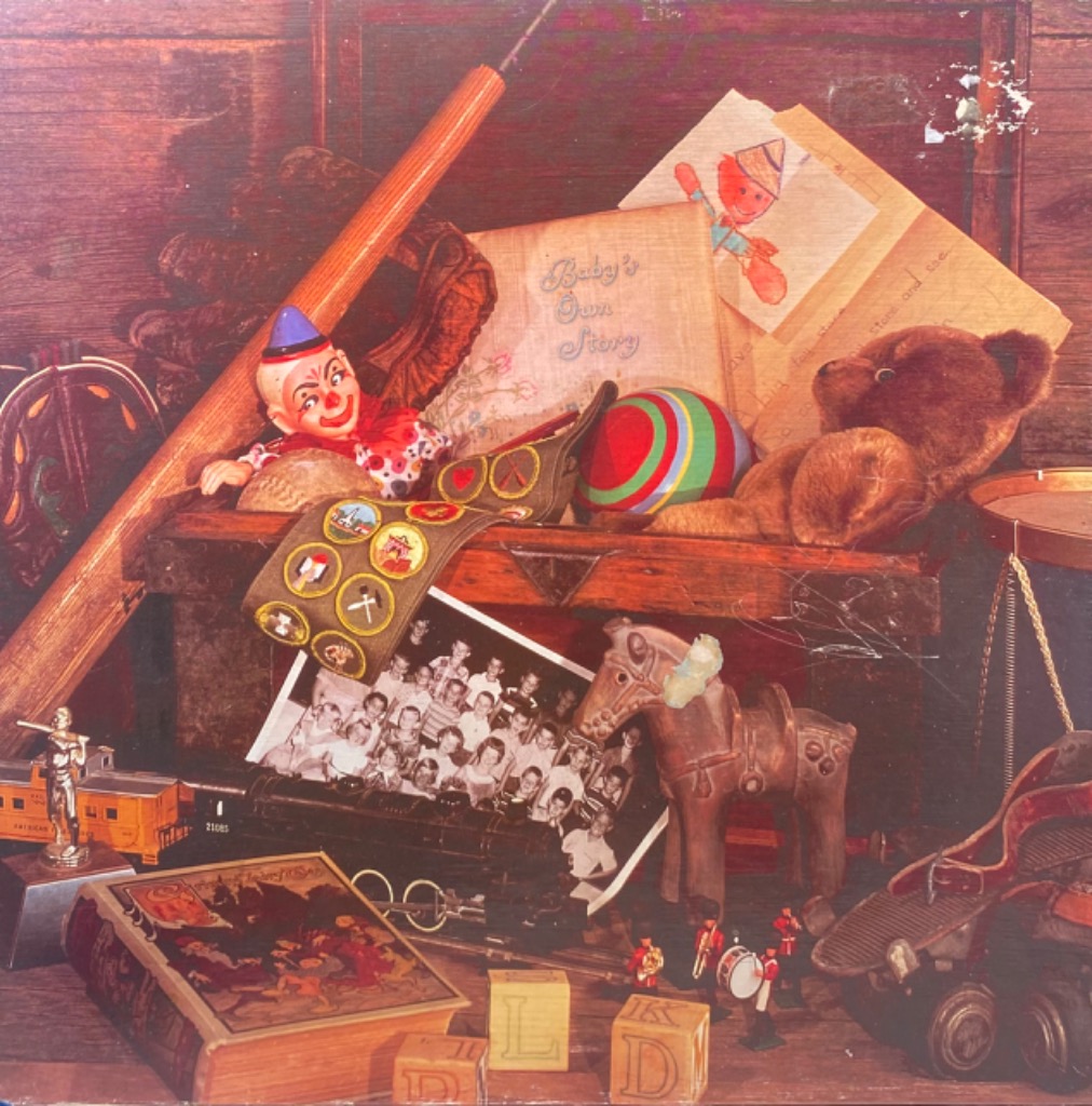 A nostalgic still life arrangement of vintage toys, a scout sash, books, and a black-and-white group photograph.