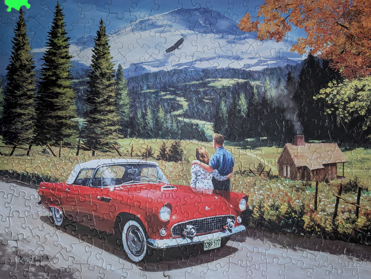 A couple standing by a red vintage convertible car overlooking a mountain landscape.