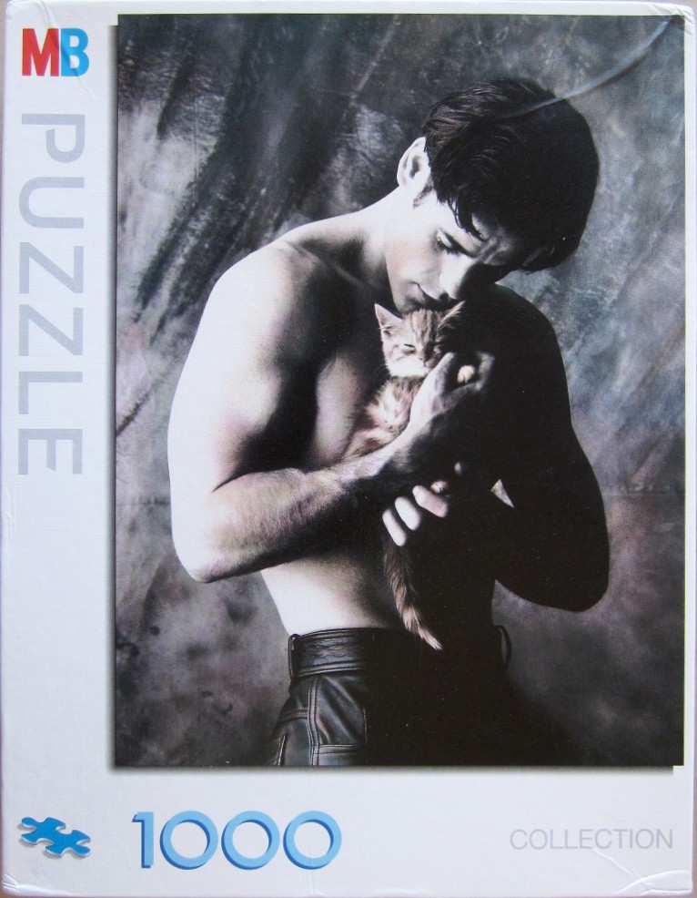 A shirtless man with dark hair tenderly holding a small tabby kitten against his chest.