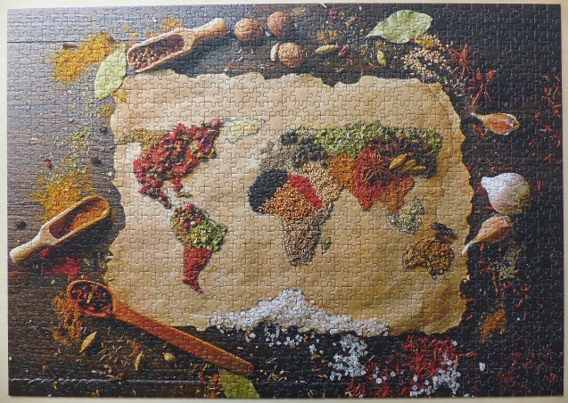 A world map created from various colourful spices on a piece of parchment paper surrounded by raw ingredients.