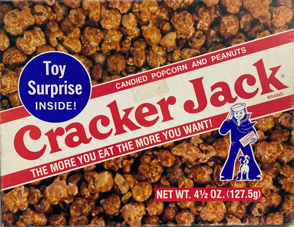 A close-up view of a Cracker Jack snack box, featuring caramel-coated popcorn and a sailor boy illustration.