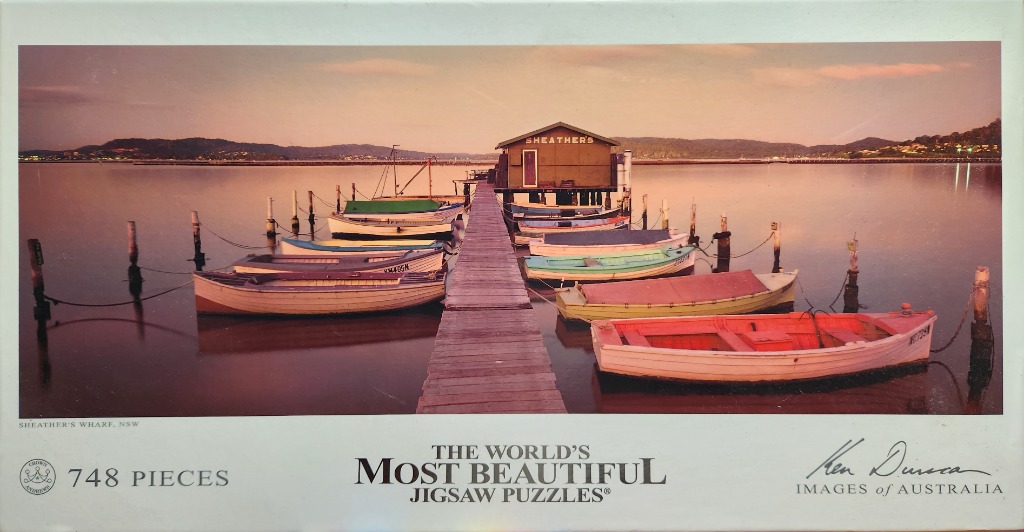 A wooden pier extending into calm water at sunset with colorful boats moored on both sides, leading to a small shack.