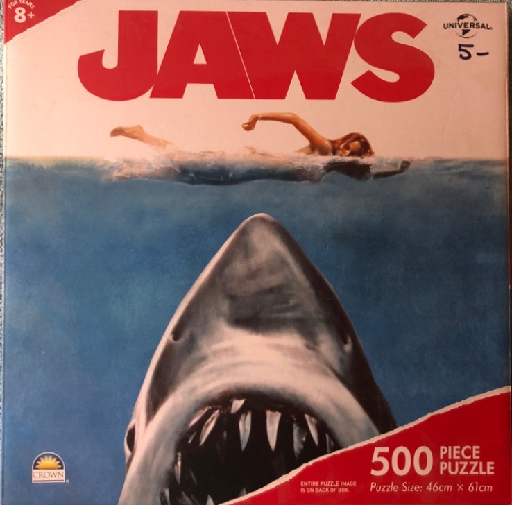 A swimmer on the surface of the ocean above a massive, shark emerging from the depths.