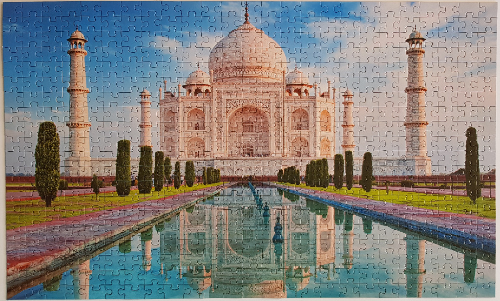 The Taj Mahal at sunrise with its reflection in a long, rectangular garden pool, framed by tall, slender cypress trees.
