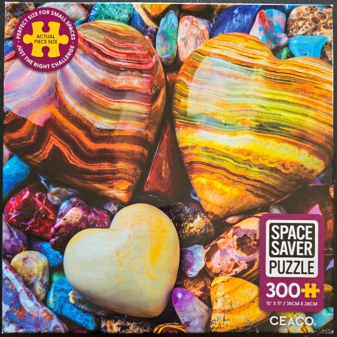 Three smooth, polished heart-shaped stones resting on a bed of colorful scattered river rocks and crystals.