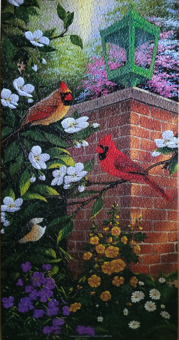 Two vibrant red cardinals perched in a lush garden beside a brick wall with a green lantern.