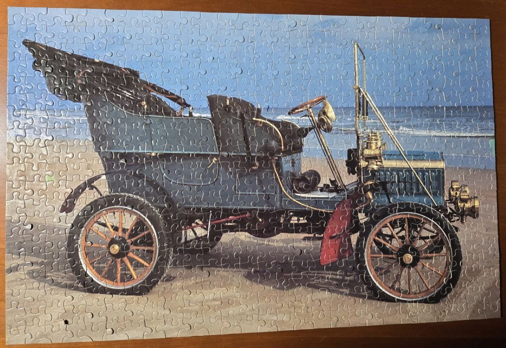 An antique blue touring car parked on a sandy beach by the ocean.