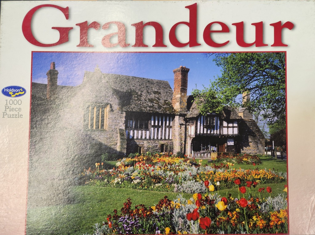 A stone and timber-framed English manor house with a vibrant spring flower garden in the foreground.
