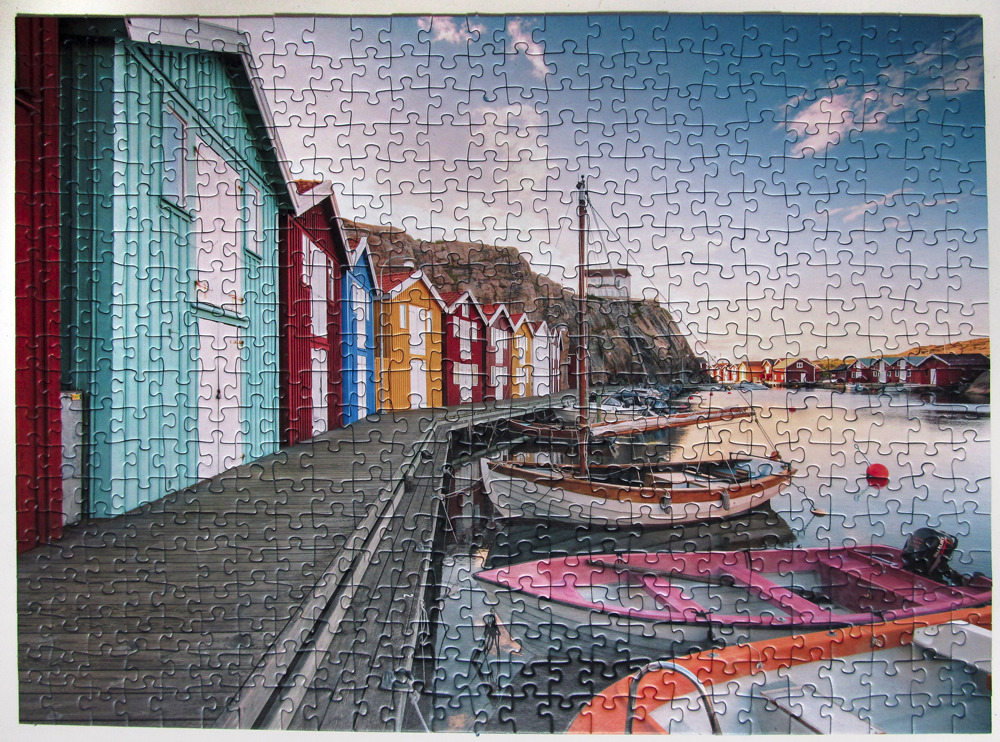 A row of colorful seaside huts along a wooden pier with small boats moored in calm water.