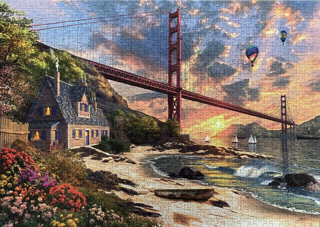 A cozy stone cottage on a beach beneath the Golden Gate Bridge at sunset with hot air balloons in the sky.