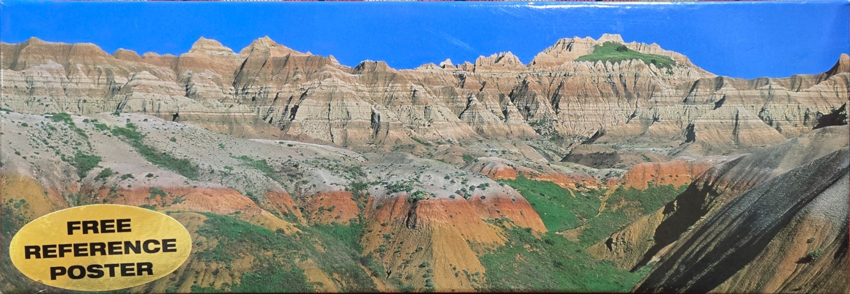 A panoramic landscape photograph of Badlands-style eroded rock formations against a vibrant blue sky.