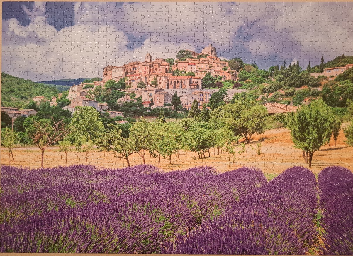 A scenic view of a Provençal hilltop village above vibrant lavender fields under a cloudy blue sky.