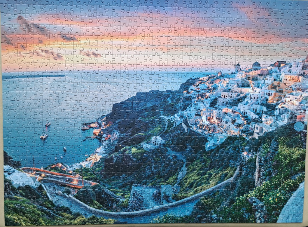 A scenic view of the town of Oia in Santorini at sunset, featuring white buildings on a cliff overlooking the Aegean Sea.