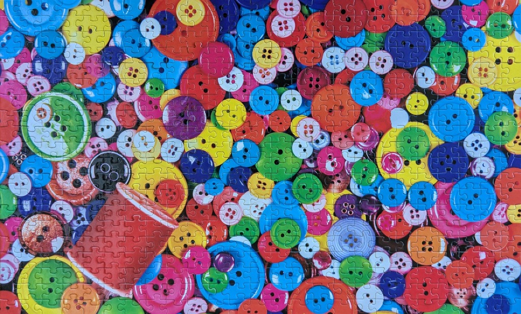 A vibrant, dense collection of colorful sewing buttons of varying sizes and a single red spool of thread.