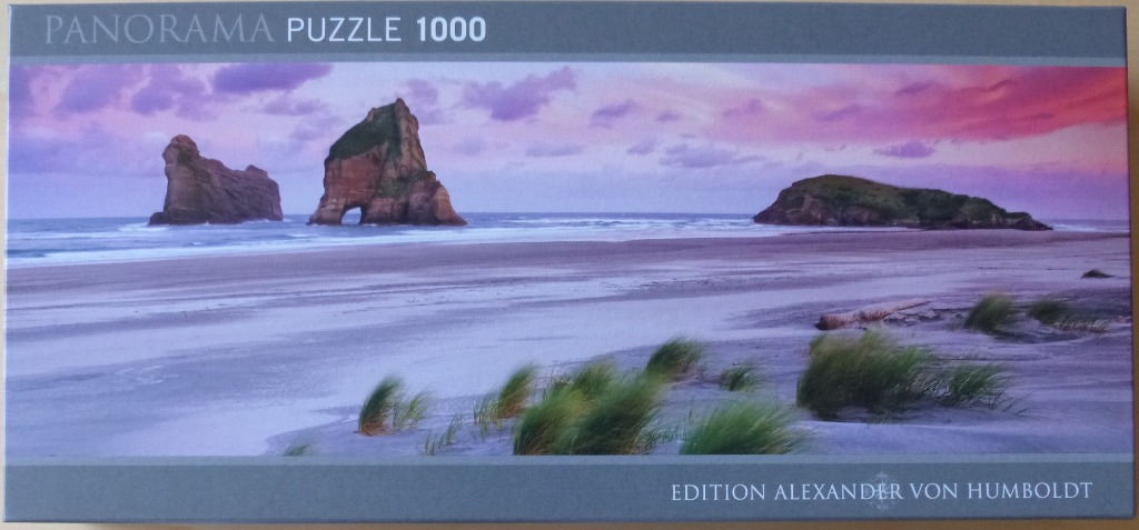 A panoramic photograph of Wharariki Beach in New Zealand at sunset, featuring iconic rock formations and dunes.