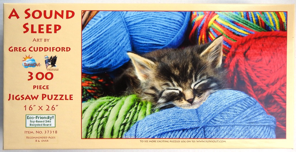 A fluffy tabby kitten sleeping soundly nestled among large, colourful balls of yarn.