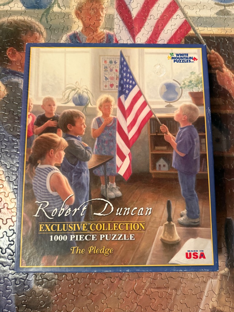 A group of children in a classroom standing to recite the Pledge of Allegiance while holding an American flag.