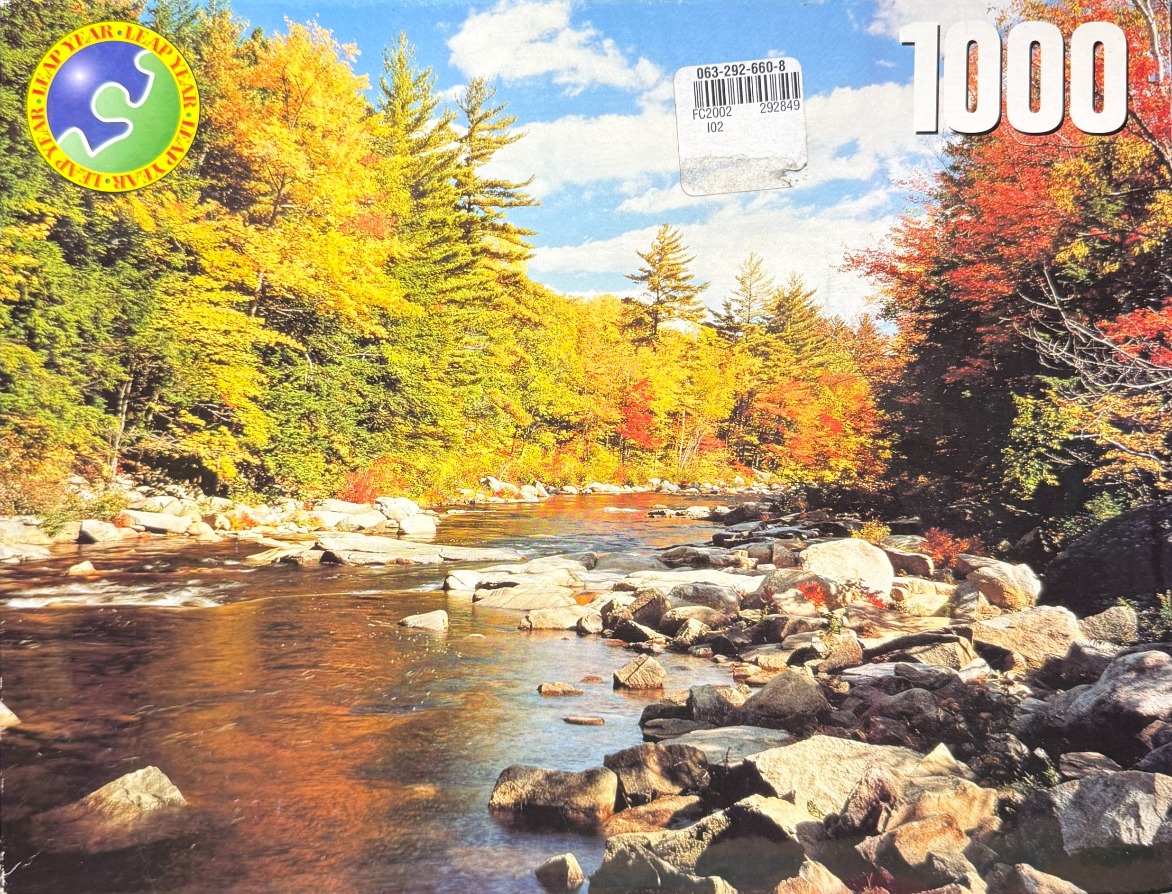 A peaceful river flowing through a colorful autumn forest under a blue sky.