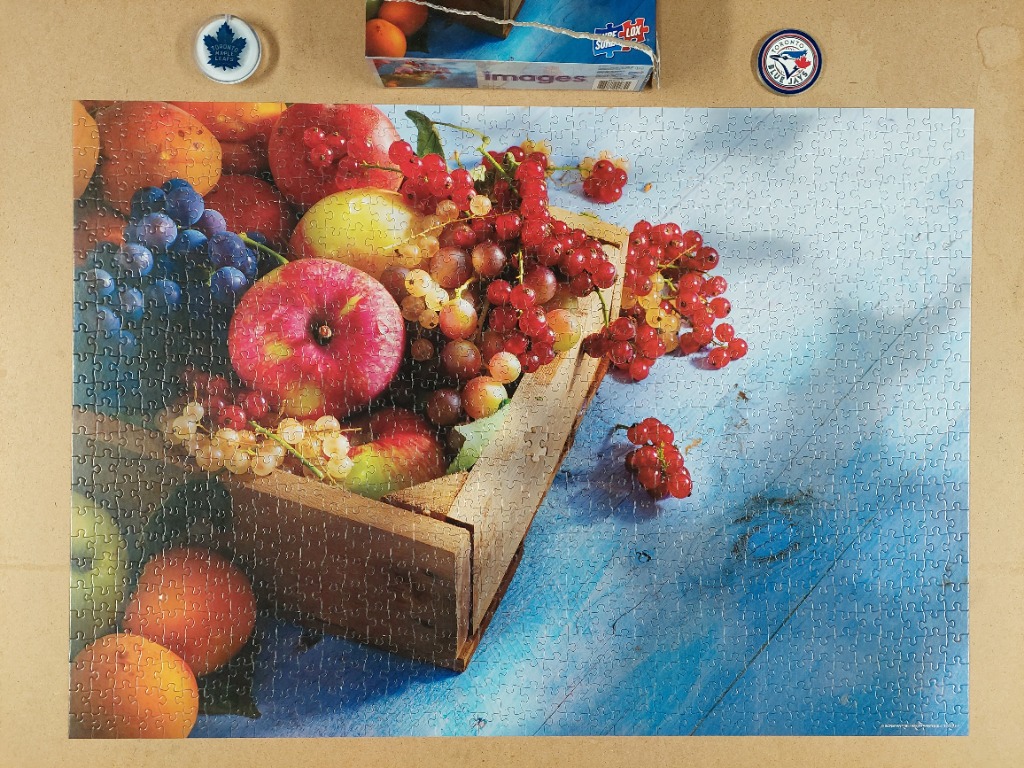 A still life photograph of mixed fruits in a wooden crate on a blue wooden surface.