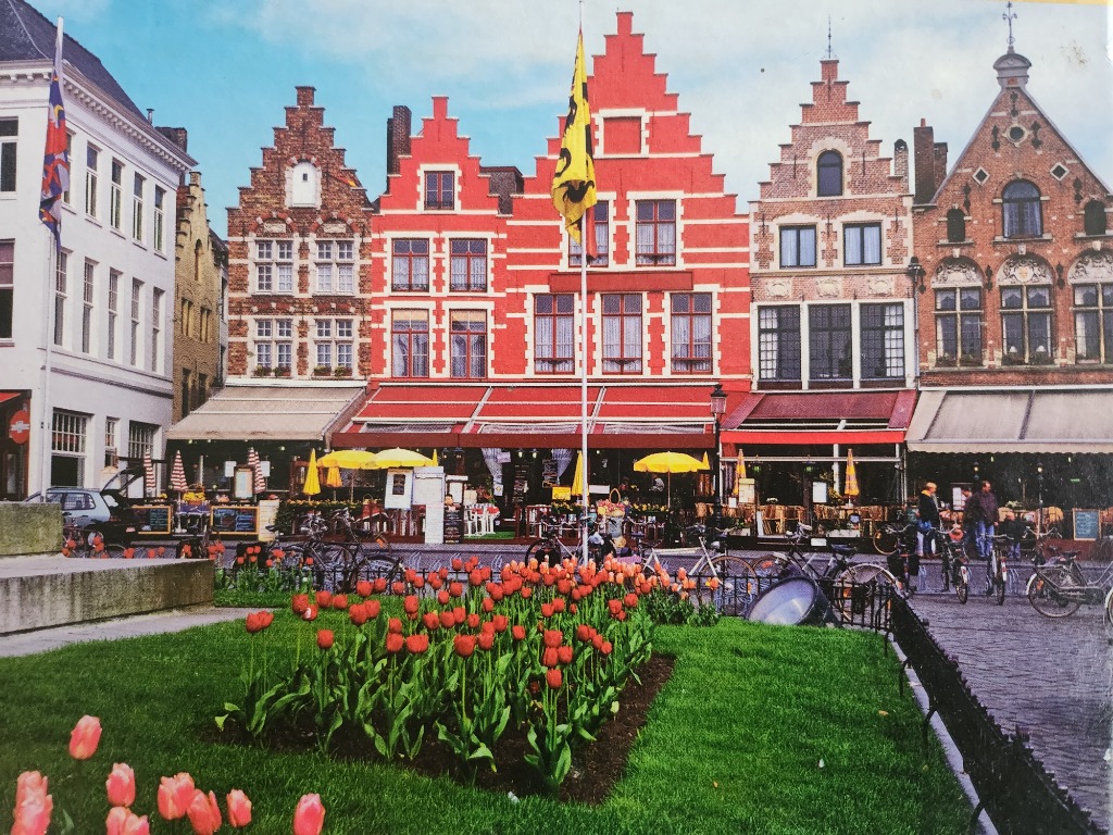 A row of historic step-gabled buildings overlooking a town square with a bed of red tulips in the foreground.