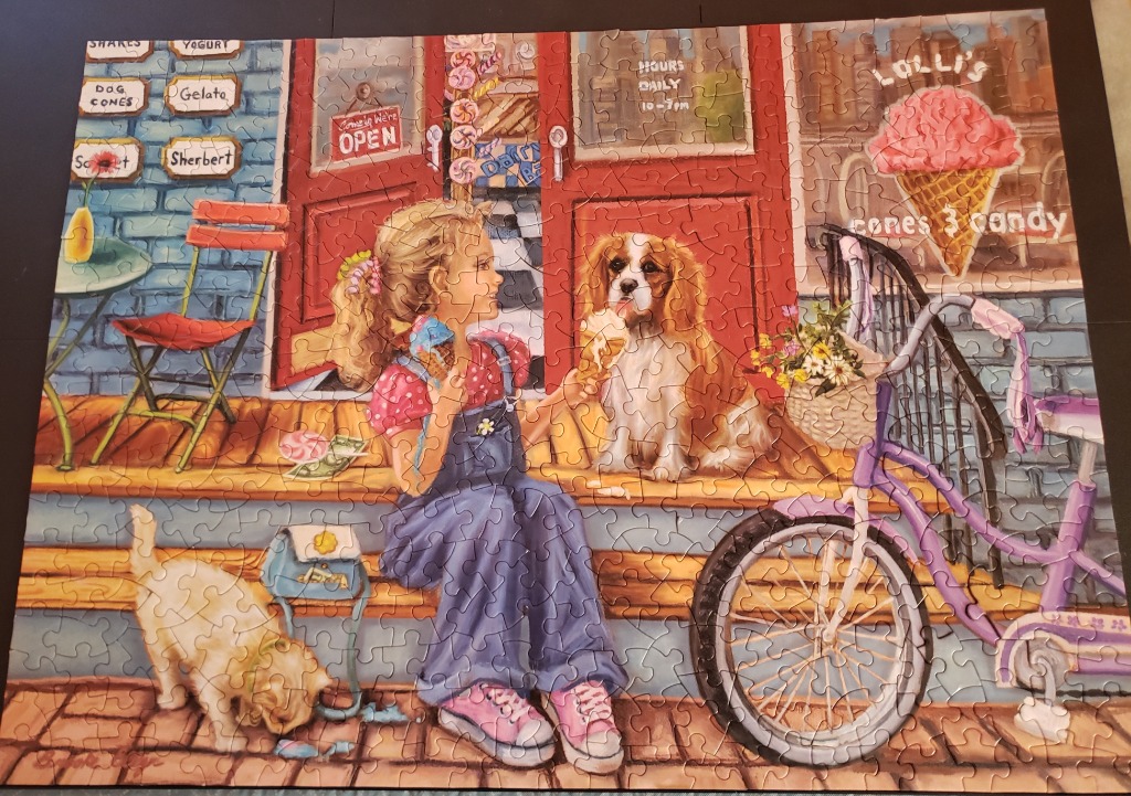 A young girl sitting on a shop porch sharing ice cream with her Cavalier King Charles Spaniel.