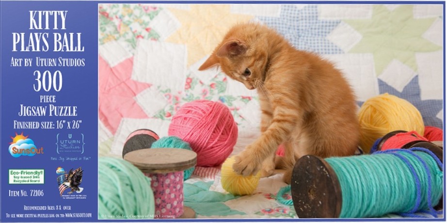 A ginger kitten sitting on a patchwork quilt playing with colorful balls of yarn and wooden spools.
