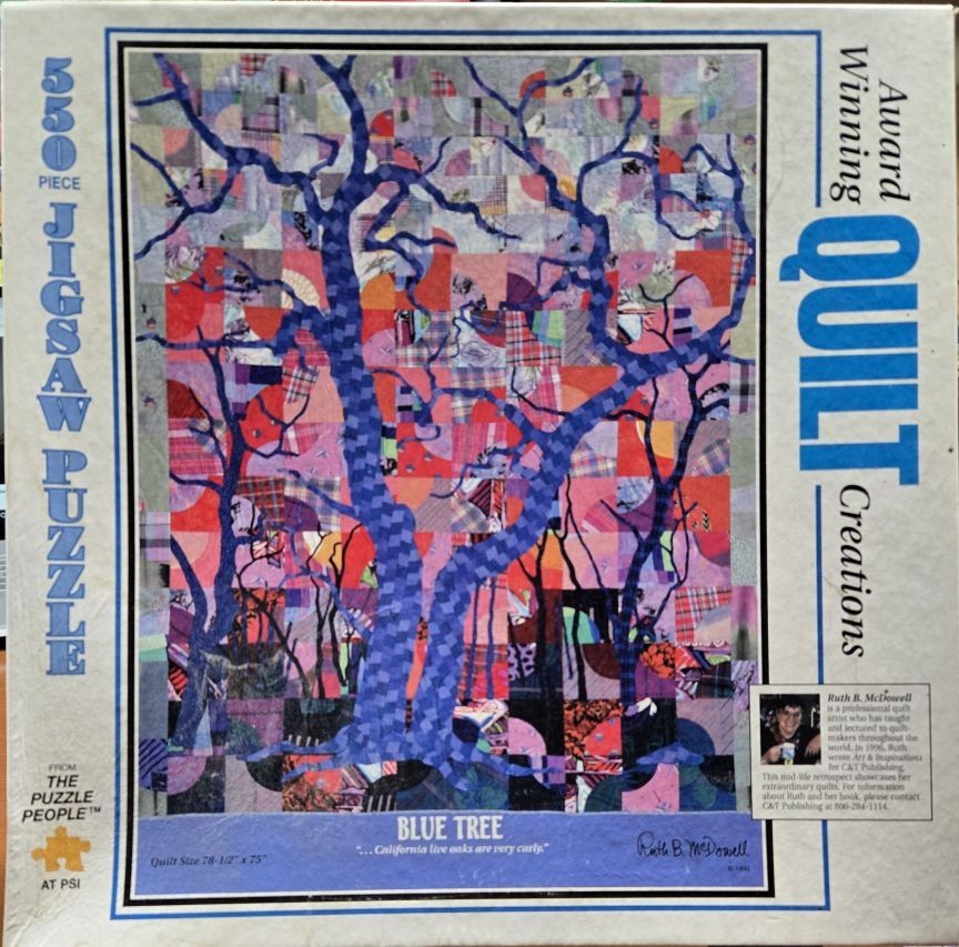 A fabric art quilt depicting a stylized blue tree against a patchwork background of various red, pink, and orange patterns.