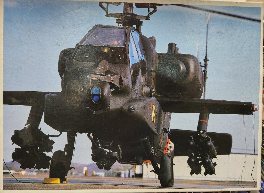 An AH-64 Apache attack helicopter parked on an airfield tarmac.