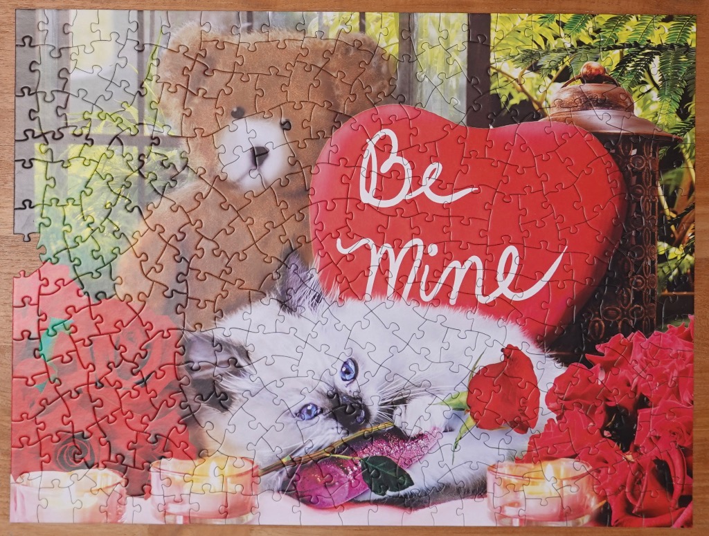 A teddy bear, fluffy kitten, and a heart-shaped sign reading Be Mine surrounded by roses and candles.
