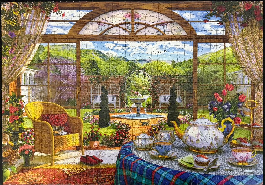 A sun-drenched sunroom overlooking a lush garden with a tea set on a table and a cat sleeping in a wicker chair.