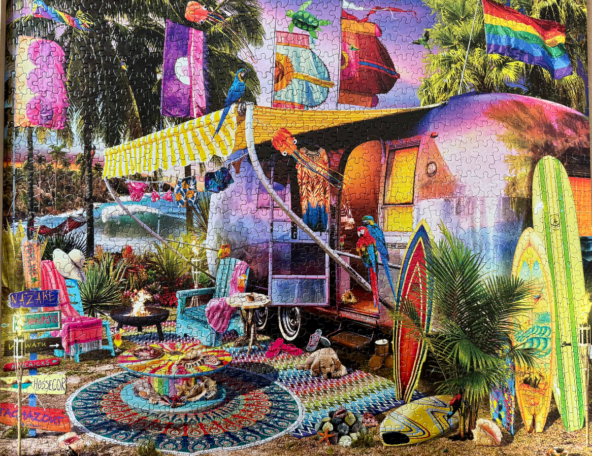 A colourful camper van parked on a tropical beach at sunset, surrounded by surfboards, a campfire, and beach decor.
