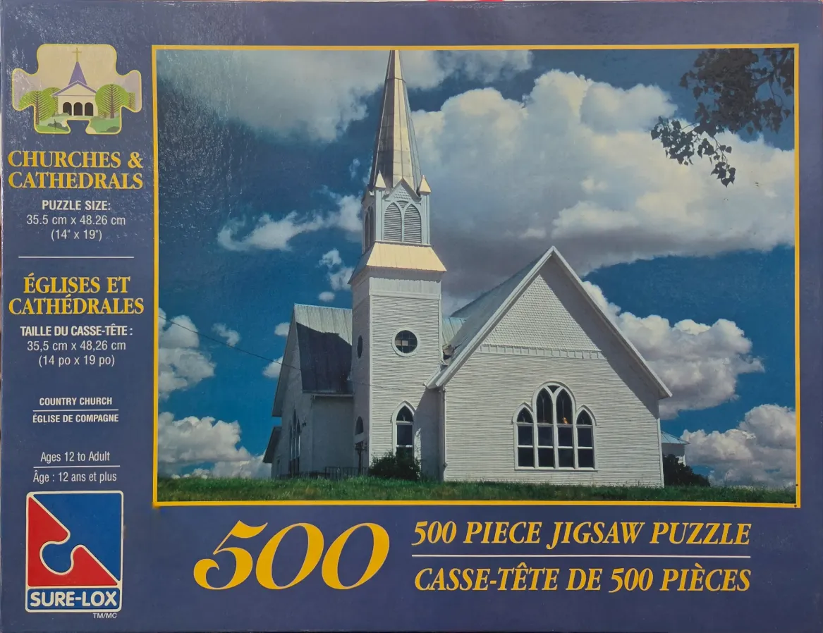 A white country church with a steeple under a bright blue sky with large, fluffy white clouds.