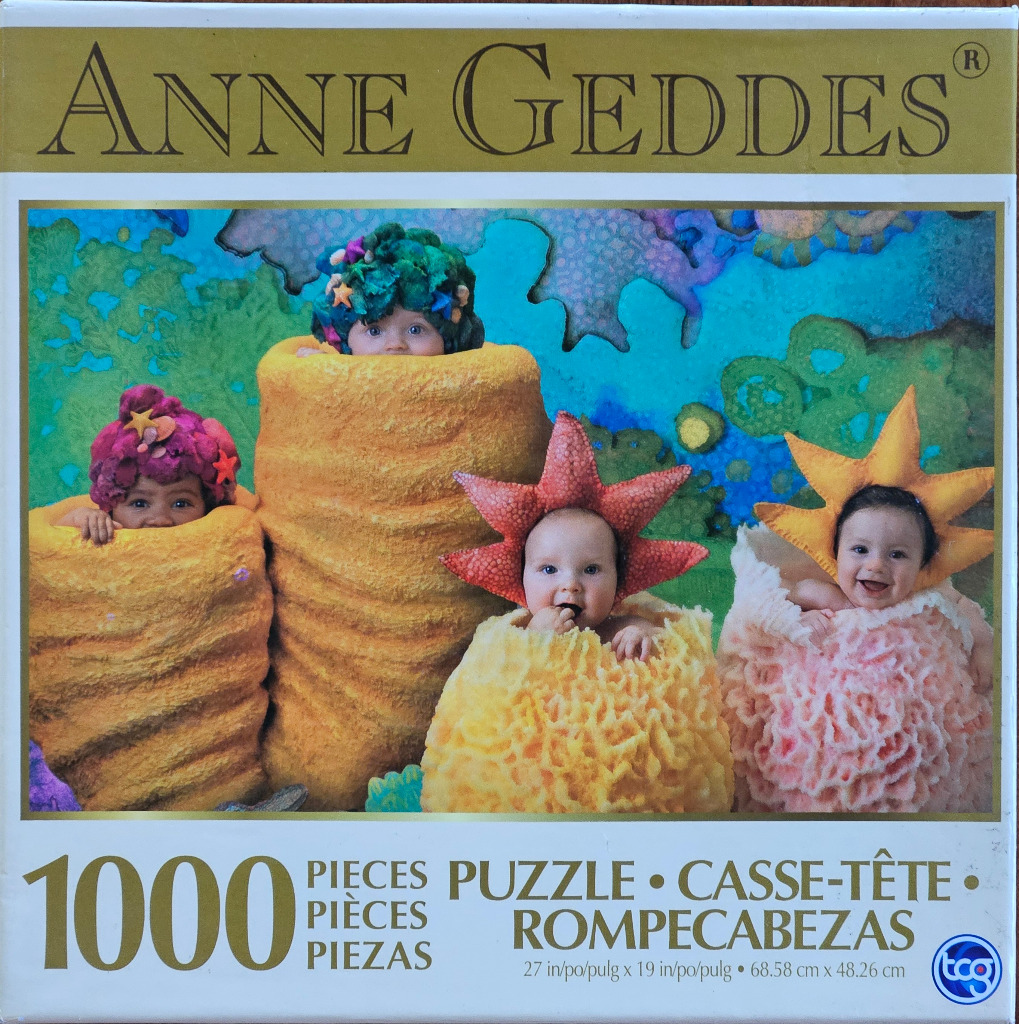 Four infants dressed as underwater creatures, including sea sponges, sea stars, and coral, against a blue background.