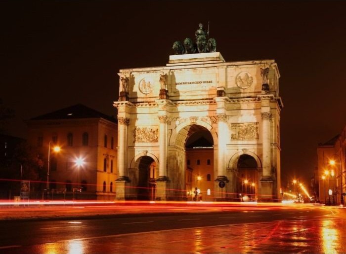The Siegestor monument in Munich illuminated at night with light trails from passing traffic.